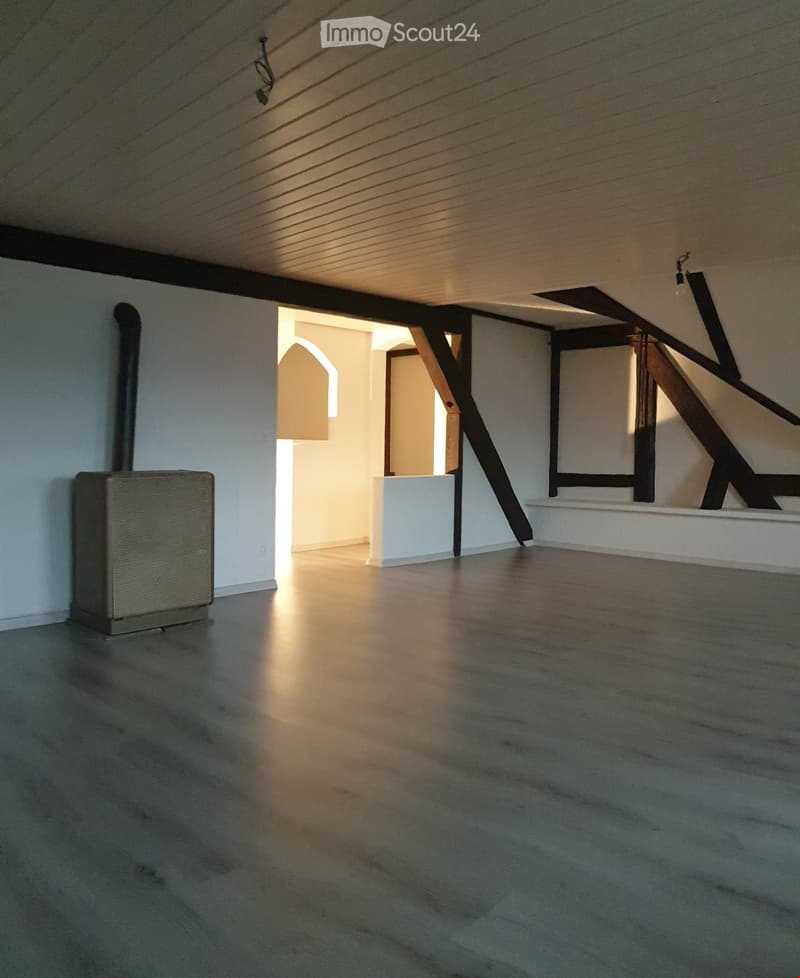 Empty room with wooden floor, white walls, exposed wooden beams, and a small radiator on the left side.