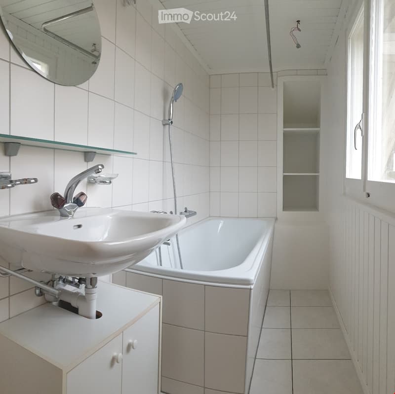 Modern bathroom with white tiles, a sink, bathtub, mirror, and built-in cabinet.