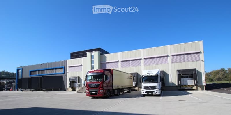 Modern industrial building with large garage doors, two trucks parked in front, clear blue sky background.