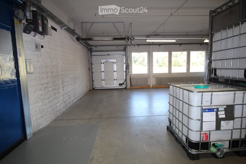Empty garage with white brick walls, large windows, and a large metal storage container on the right side.