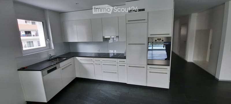 Modern kitchen with white cabinets, black countertops, stainless steel appliances, and a large window offering a view of the building outside.