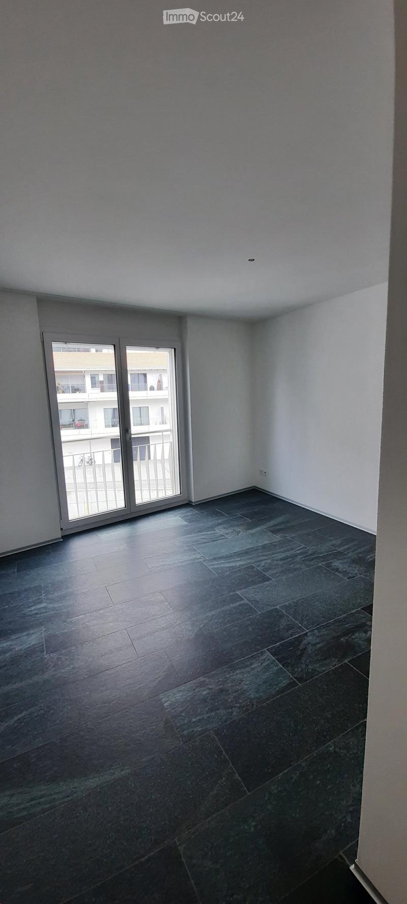 Empty room with dark tiled floor and white walls, featuring a large sliding glass door leading to a balcony.
