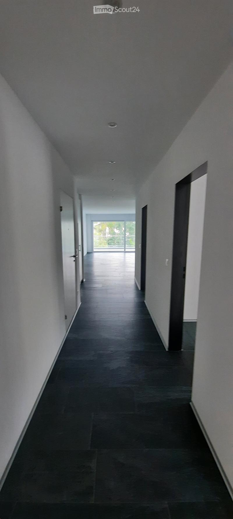 Empty hallway with dark tiled flooring, white walls, and recessed lighting. Doors on both sides lead to other rooms.