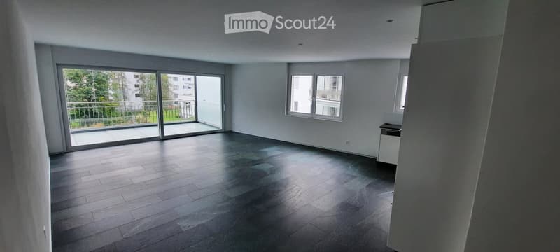 Empty room with wooden flooring, large sliding glass doors leading to a balcony, and white walls.