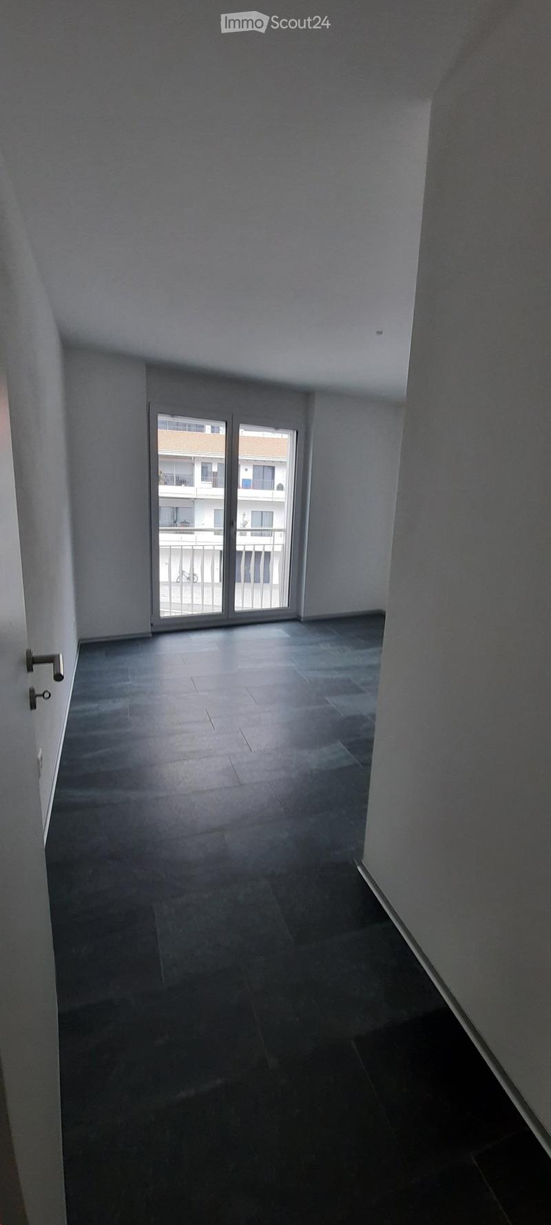 Empty room with dark tiled floor, white walls, and a sliding glass door leading to a balcony.
