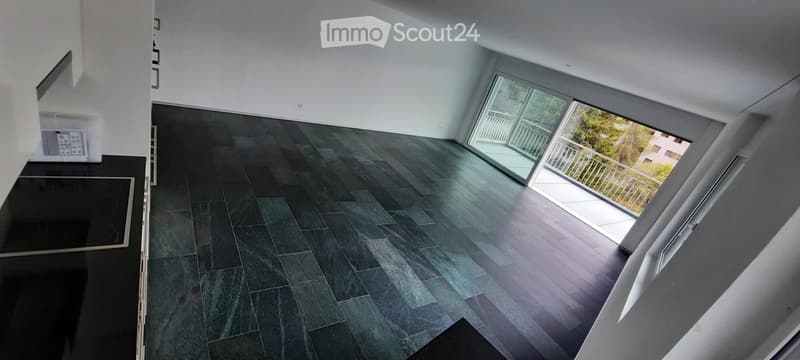 Empty room with dark tiled floor, white walls, large windows, and a balcony with a metal railing.