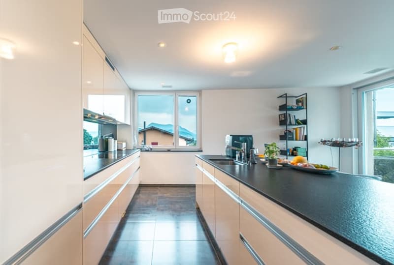 Modern kitchen with white cabinets, black countertop, stainless steel appliances, and a view of the mountains through large windows.