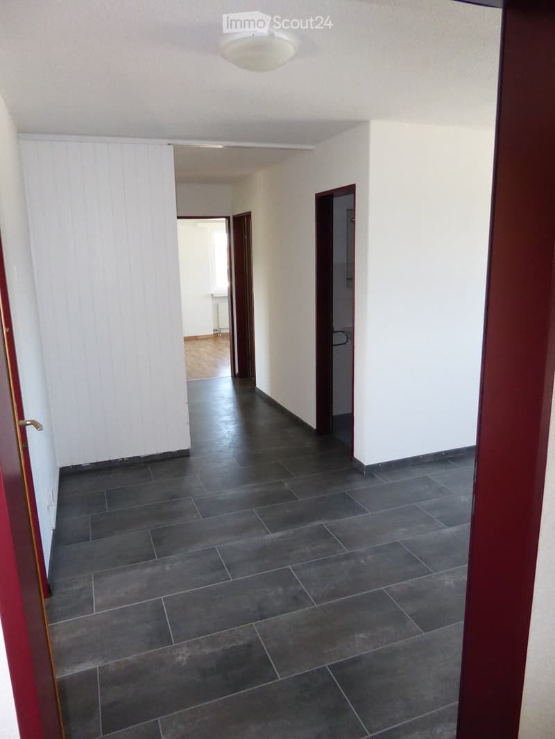Empty hallway with dark tiled flooring, white walls, and several doors leading to other rooms.