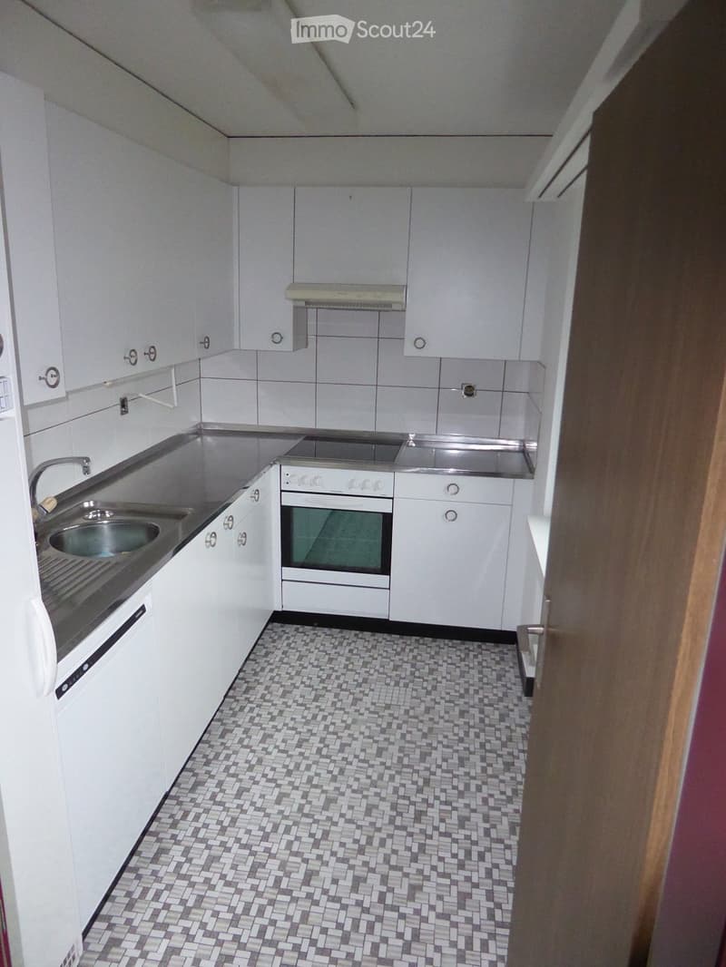 Modern kitchen with white cabinets, stainless steel sink, oven, and tiled floor.