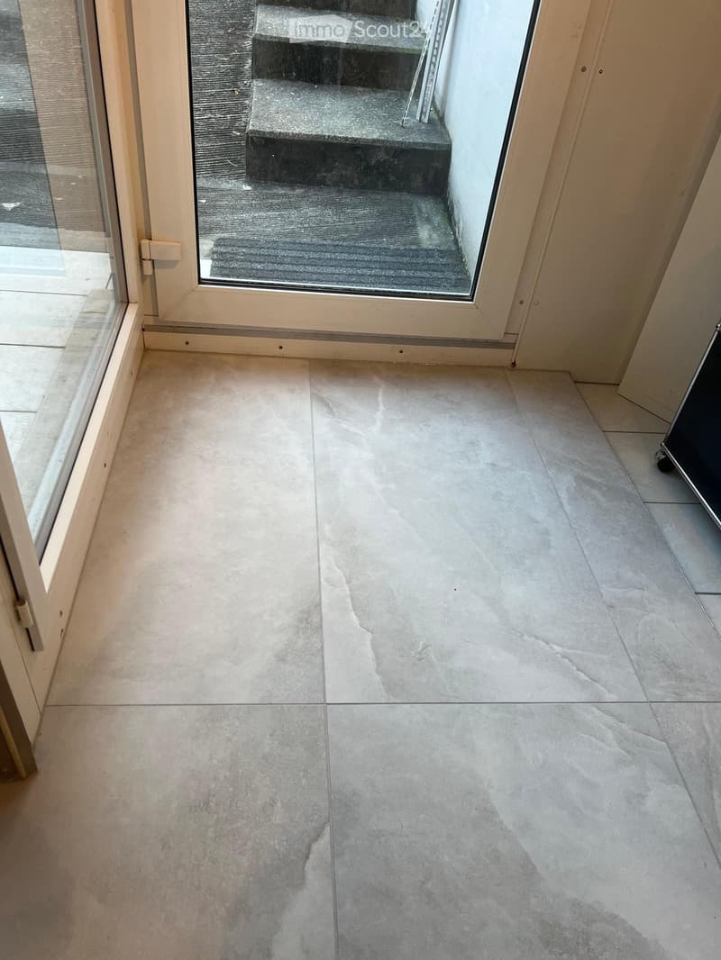 Empty hallway with light-colored tiled flooring and a large glass door leading to an outdoor area.