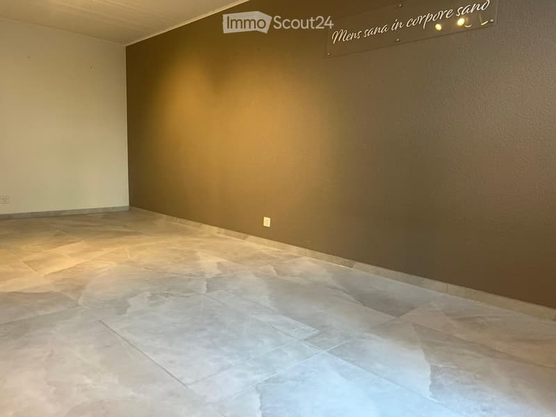 Empty room with beige tiled floor and brown walls, featuring a decorative sign on the wall and recessed lighting.
