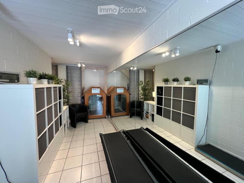 Modern, well-lit room with white brick walls, tiled floor, and a large mirror. Features include a black chair, small table, decorative cabinet, and potted plants.