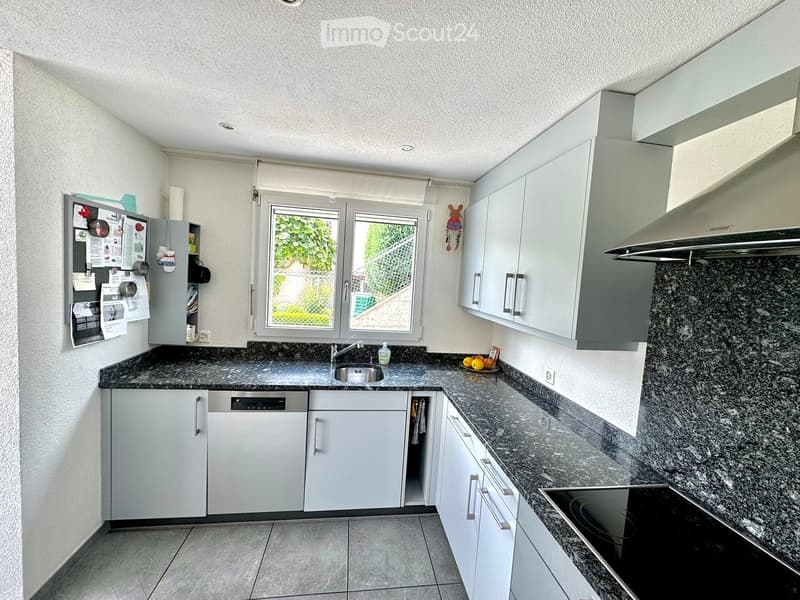 Modern kitchen with white cabinets, granite countertops, and stainless steel appliances, including a sink, dishwasher, and electric stove. A window offers a view of greenery outside.
