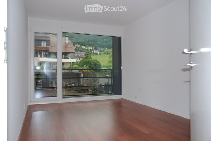 Empty room with wooden flooring, white walls, and large windows offering a scenic view of the surrounding area.