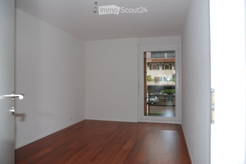 Empty hallway with wooden flooring, white walls, and a glass door leading to an outdoor area.