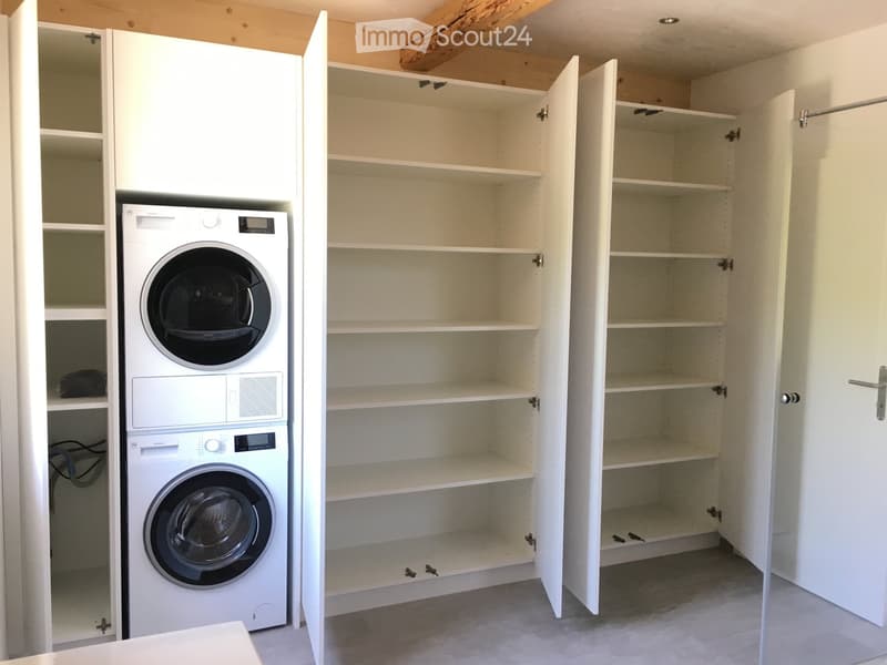 Laundry area with a white washing machine and built-in white cabinets with open shelves.