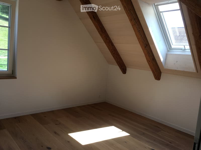 Empty attic room with wooden floors, exposed wooden beams, and skylight windows allowing natural light to enter.