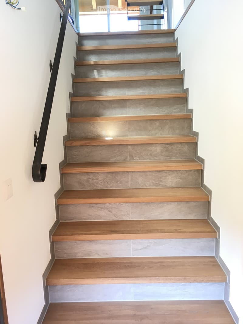 Staircase with wooden steps and a metal railing, leading upwards with a modern design.