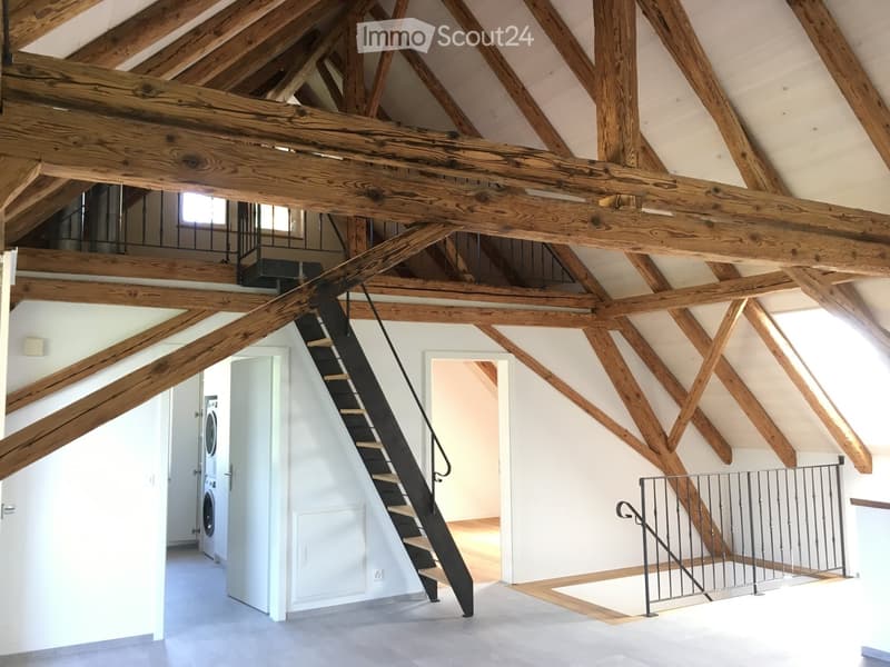 Open attic space with exposed wooden beams, a staircase leading to an upper level, and a washing machine in the corner.