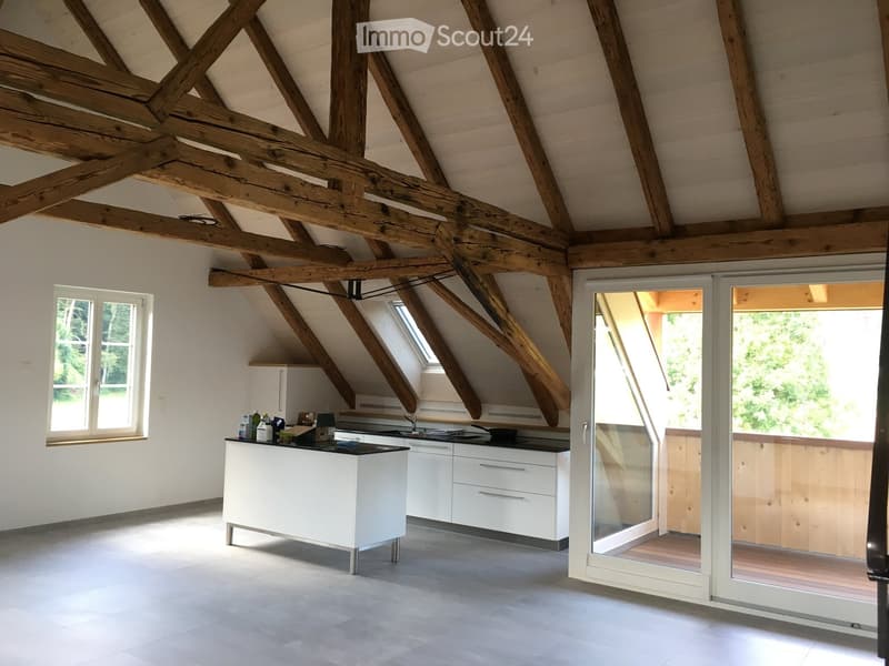 Modern kitchen with white cabinets, island, and exposed wooden beams. Large windows and sliding glass doors lead to a balcony.