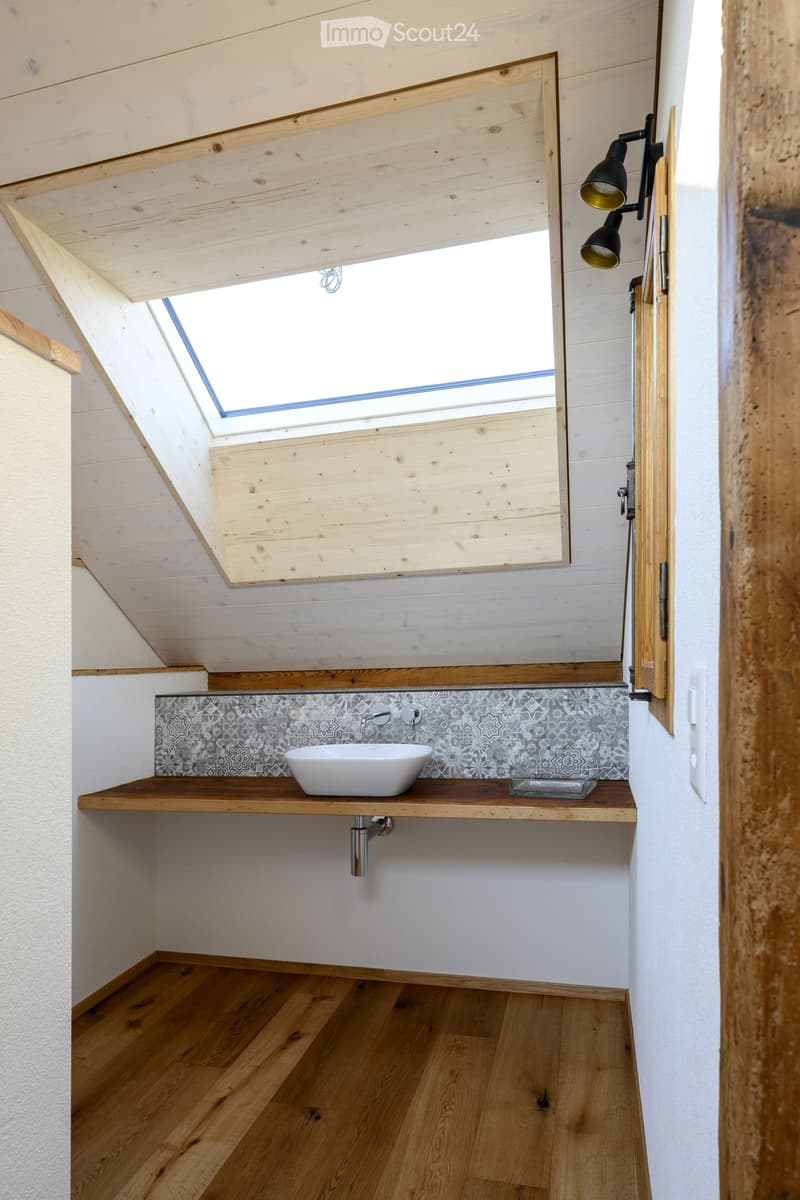 Modern bathroom with wooden ceiling and floor, white sink on wooden countertop, decorative backsplash, and wall-mounted lighting fixture.