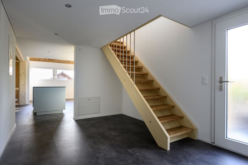 Modern hallway with a wooden staircase featuring metal railings, dark grey tiled floor, white walls, and a grey cabinet on the left side.