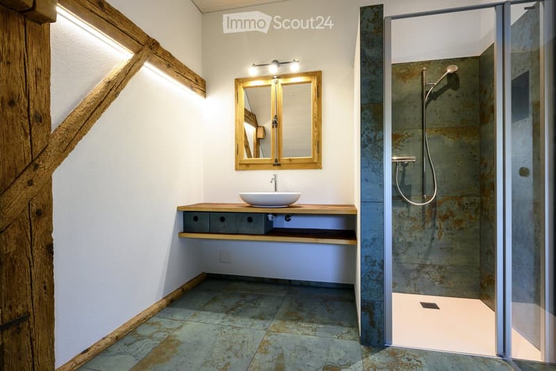 Modern bathroom with a wooden vanity, white sink, double mirror, and a glass-enclosed shower with a modern showerhead.