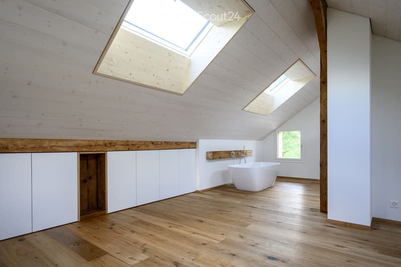 Modern bathroom with wooden floors, white walls, and a freestanding bathtub. Features built-in white cabinets and skylight windows for natural light.