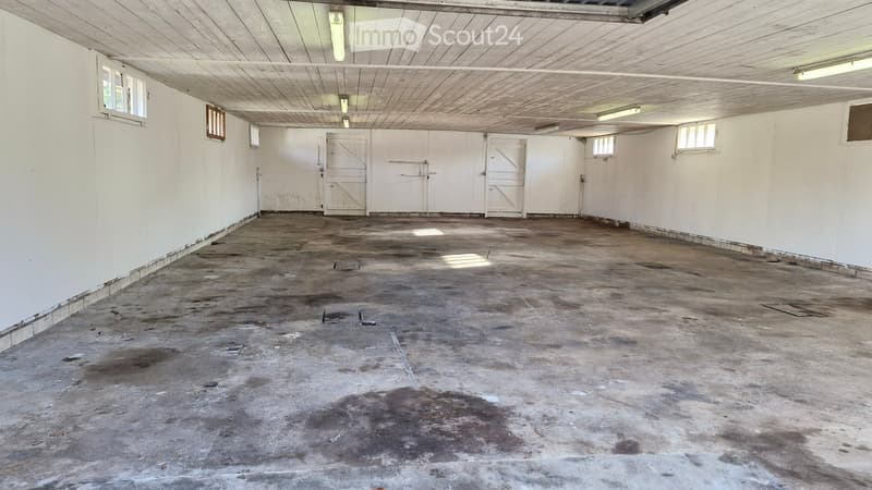 Empty garage with concrete floor, white walls, wooden ceiling, and multiple doors.