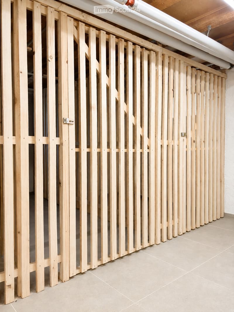 A hallway with a wooden slatted partition wall, beige tiled floor, and exposed wooden beams on the ceiling.