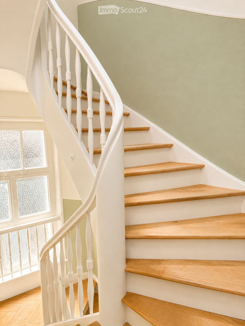 Spiral staircase with wooden steps and white balustrade, light green walls, frosted glass windows on the left side.