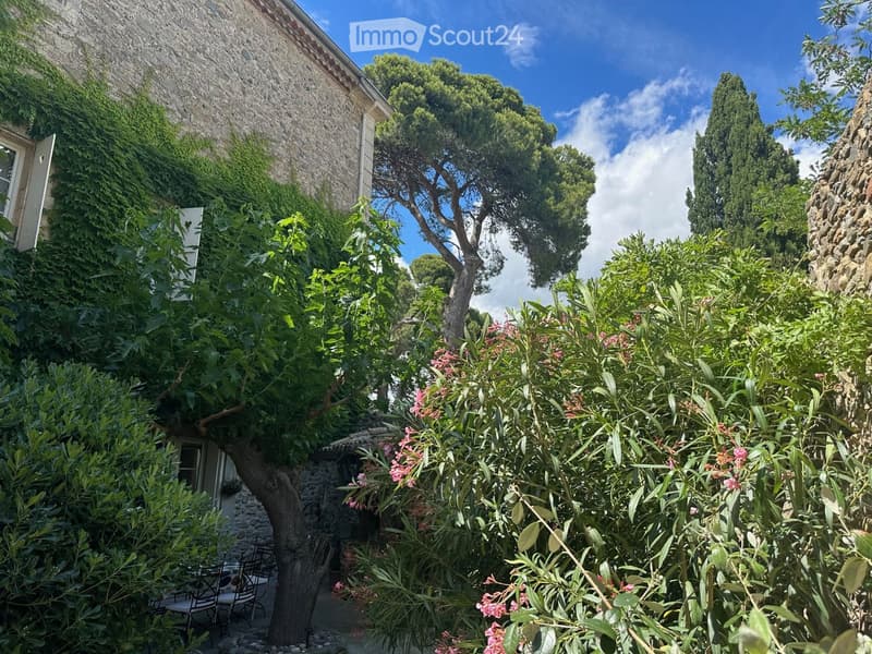 Garden area with stone walls, lush greenery, flowering plants, and a small seating area with a table and chairs.