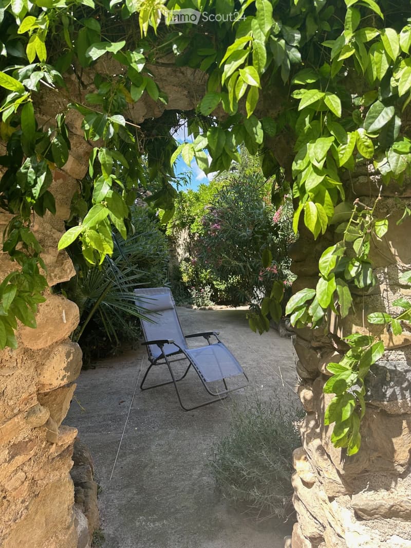 A narrow stone pathway lined with lush greenery and a single lounge chair placed on the gravel.