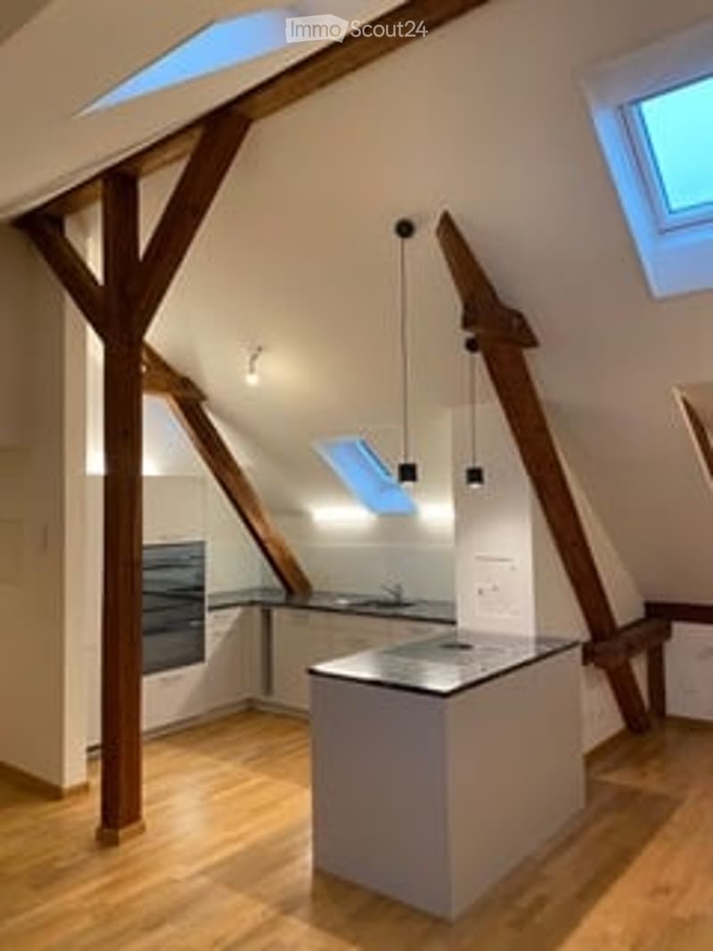 Bright, open-plan attic kitchen with exposed wooden beams, skylights, and modern appliances.