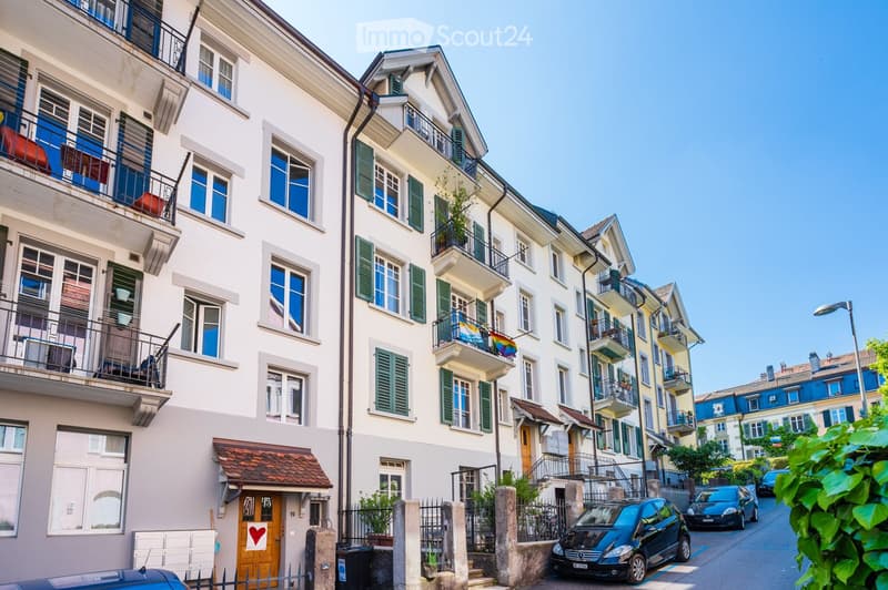 Multi-story residential building with balconies, green shutters, and a small entrance with a heart symbol on the door.