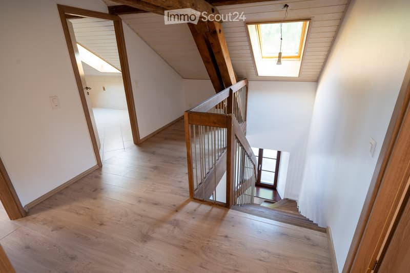 Spacious hallway with wooden flooring, white walls, and a staircase leading upwards. Features a wooden railing and a skylight providing natural light.