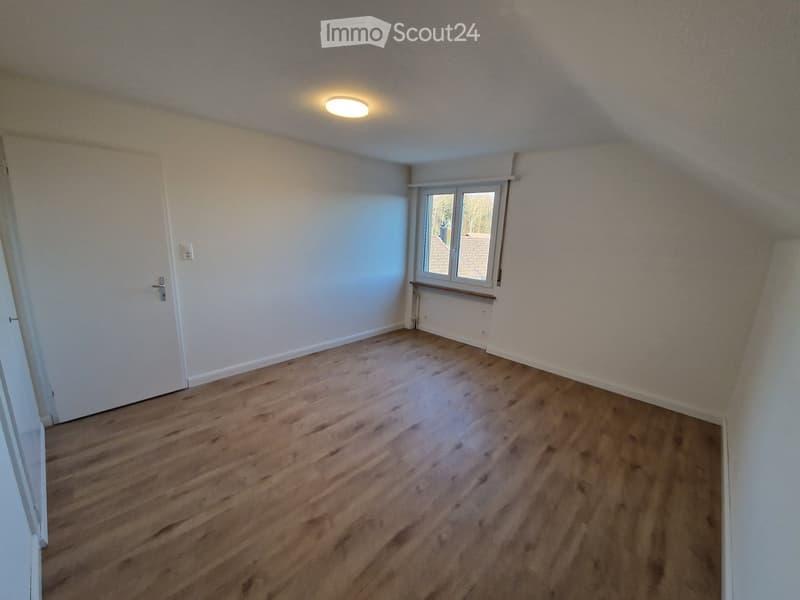 Empty room with wooden flooring, white walls, a single window, and a closed door.