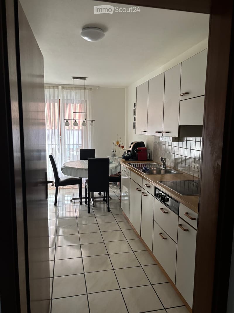 Modern kitchen with white cabinets, a dining area, and a sink. The space includes a table with chairs, a light fixture, and various kitchen appliances.