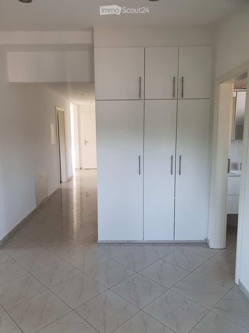 Empty room with white tiled walls, marble tiled floor, and white cabinetry along one wall. No furniture or personal items visible.