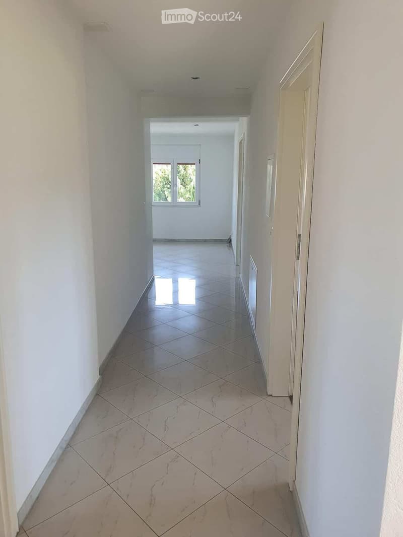 Empty hallway with white walls, tiled floor, and multiple doors leading to other rooms.