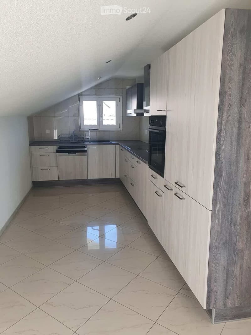 Modern kitchen with light wood cabinets, stainless steel appliances, and tiled flooring.
