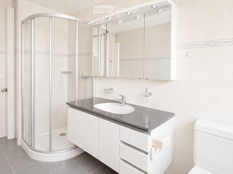 Modern bathroom with a white sink, chrome faucet, large mirror with built-in lighting, white cabinetry, and a glass-enclosed shower stall.