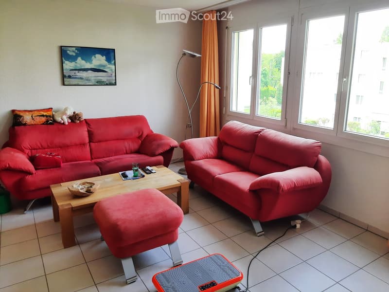 Bright living room with red sofas, a wooden coffee table, and a floor lamp near large windows.
