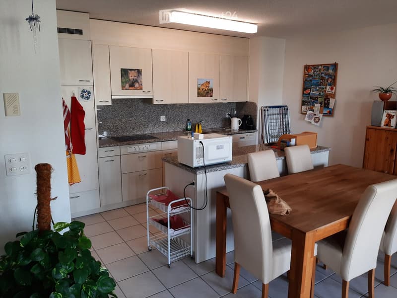 Modern kitchen with white cabinets, granite countertops, microwave, coffee maker, and a dining area with a wooden table and white chairs.
