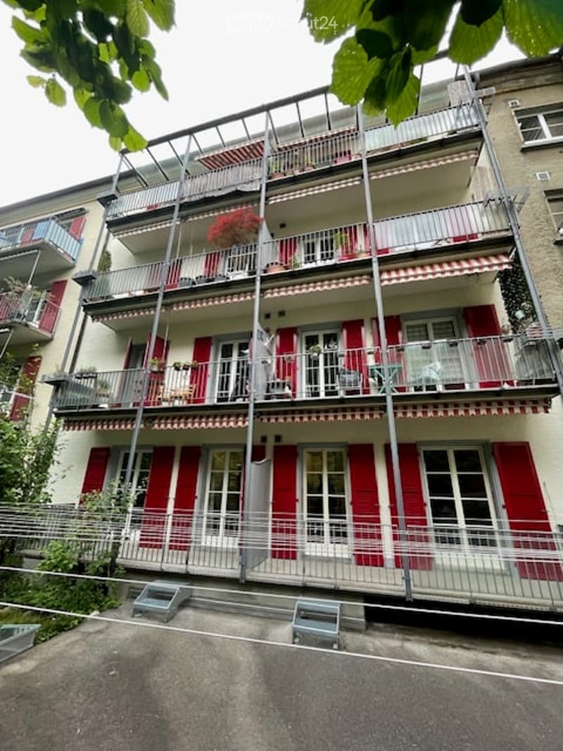 Multi-story residential building with multiple balconies, red shutters, and white railings.