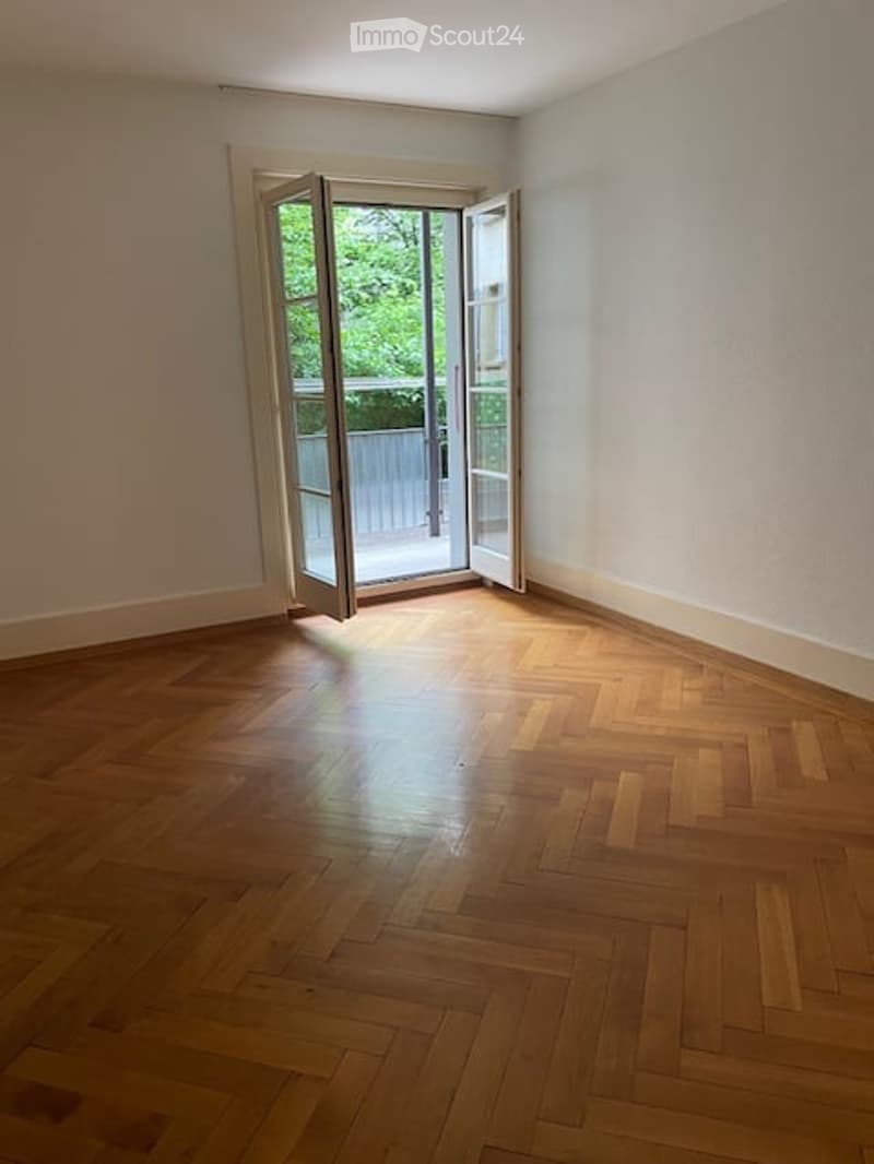 Empty room with wooden parquet flooring and large open French windows leading to a balcony or terrace area.