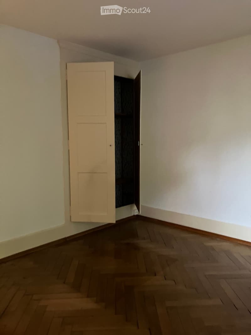Empty room with wooden flooring and light-colored walls, featuring an open door leading to another space.
