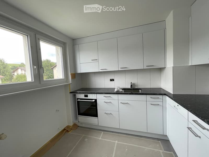 Modern kitchen with white cabinets, black countertops, and stainless steel appliances including an oven and sink.