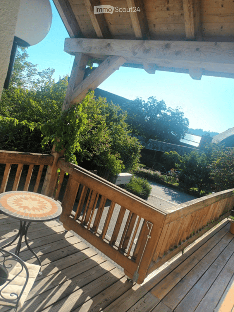Wooden balcony, round table, wooden railings, green plants, clear sky