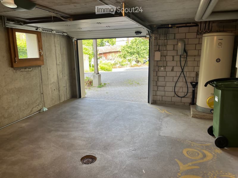 {"type": "Garage", "objects": [], "visible_features": [], "description": "Empty garage with concrete floor, open garage door, water heater, and a green trash bin. The floor has a painted snail design."}